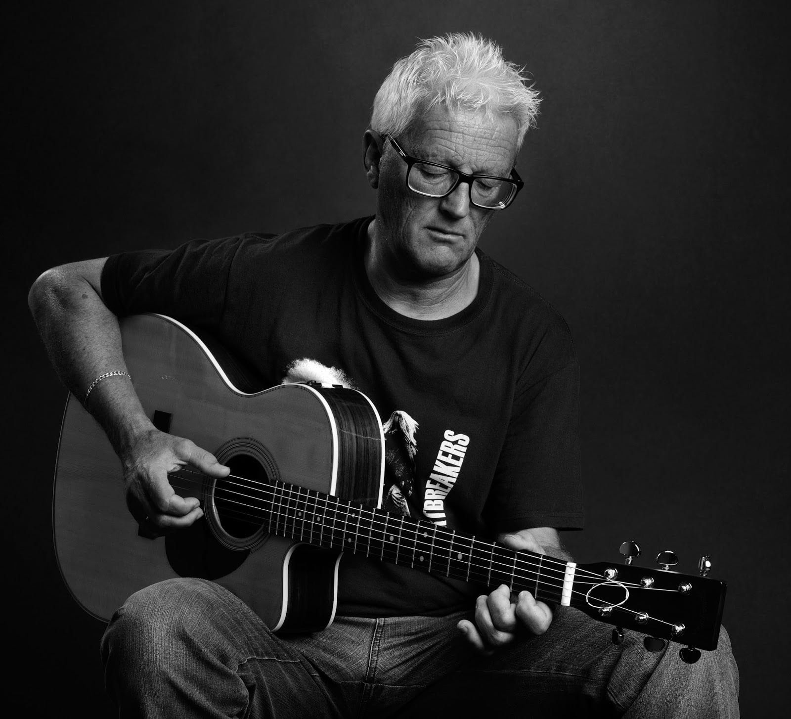 Schwarzweiß: Gitarrenspiel im Studio, weißes Haar, Brille