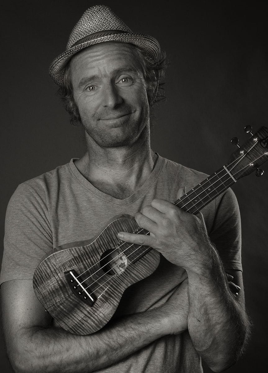 Schwarzweiß-Portrait einer lächelnden Person mit Hut, die eine Ukulele vor der Brust hält